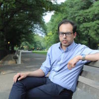 A man sitting on a blench. He's wearing glasses