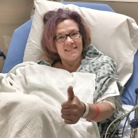 A picture of the writer in a hospital bed, giving a thumbs up.