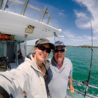 A picture of a young woman and older man on a boat, standing next to a fishing pole.