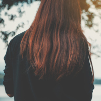 A picture of the back of a woman's head, as she faces a body of water.