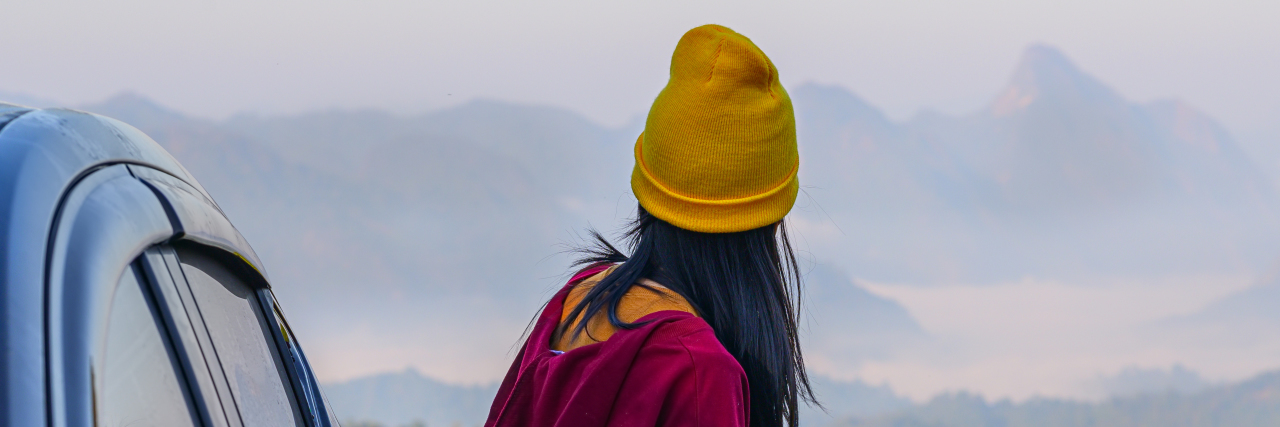 My Positive First Experience in a Psychiatric Hospital as a Teen young woman in a yellow beanie and red jacket standing outside her car looking at the mountains