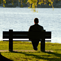 Young man sitting alone on park bench by the water.