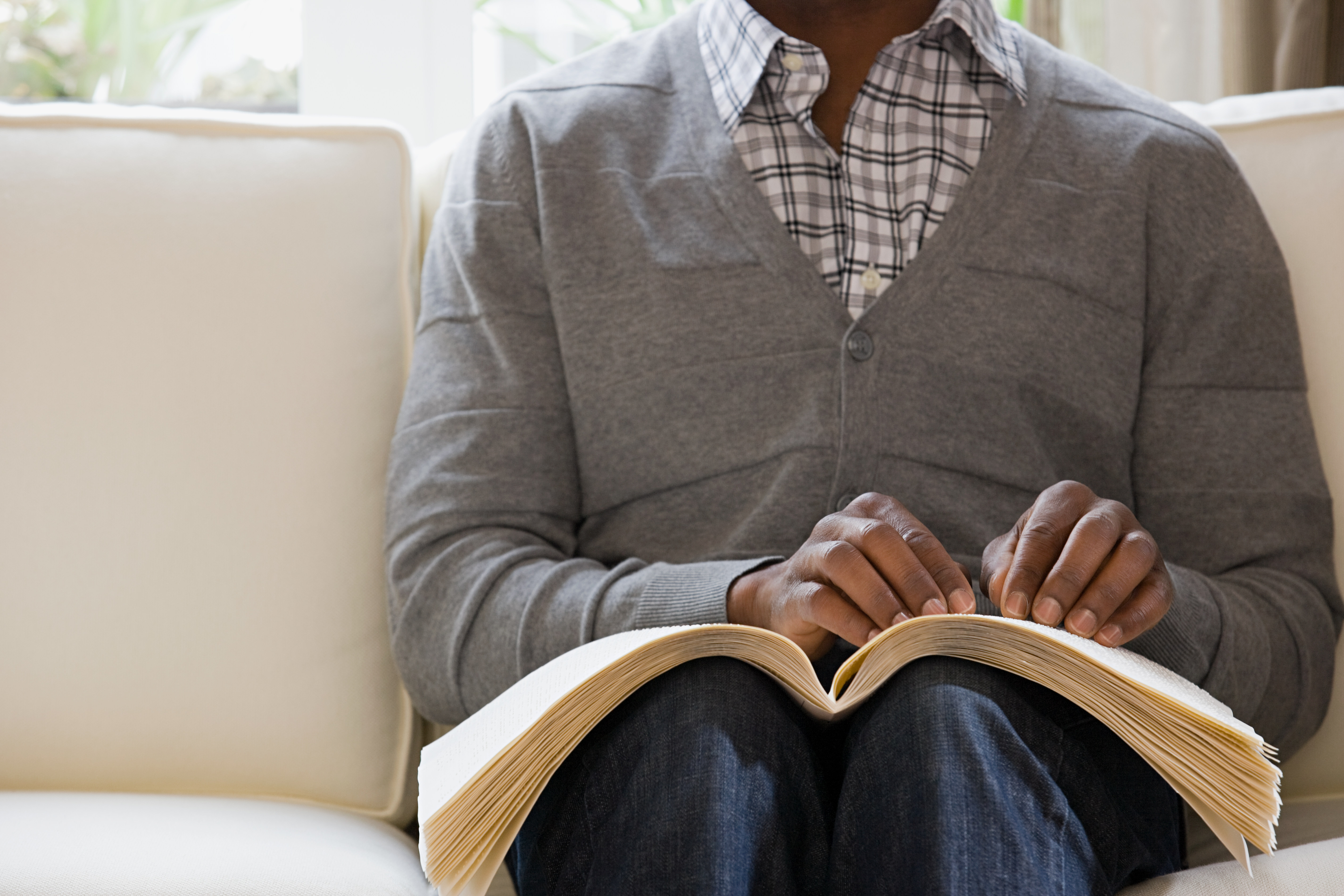 African American blind man reading a braille book.