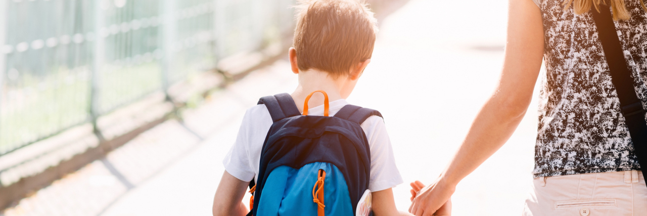 The Guilt Mothers Can Feel When Living With a Chronic Illness A little boy holding his mom's hand while they walk to school with his backpack on.