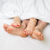 Feet of a couple in bed under a white blanket.