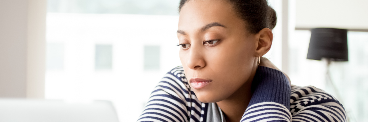 Why It's Hard to get Disability Benefits for Fibromyalgia A woman looking at her computer, wearing a serious facial expression.