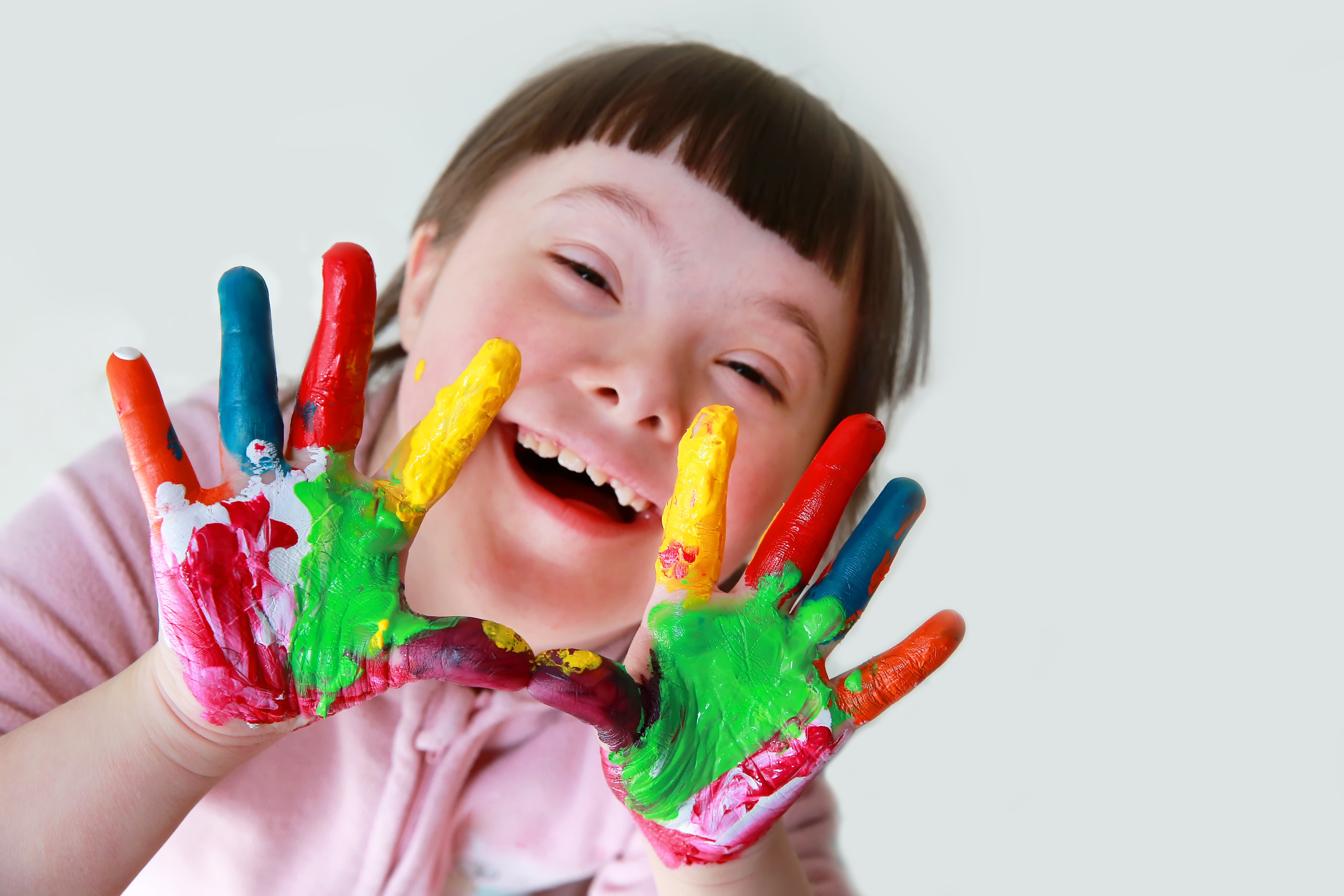 Girl with Down syndrome. Her hands are covered in colorful paint.