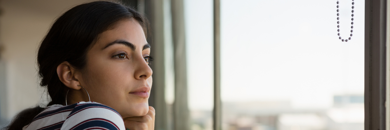 Thoughtful young beautiful woman looking through window at office
