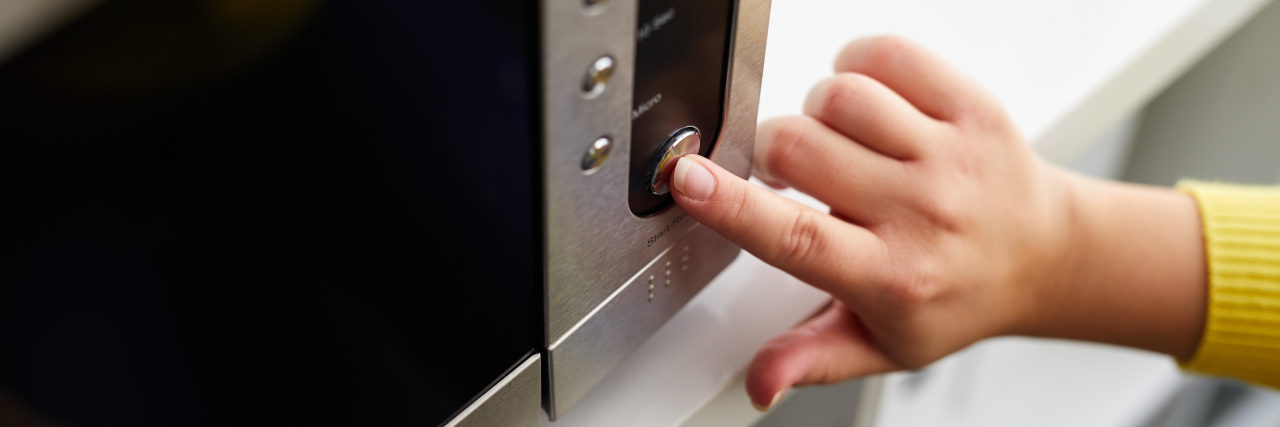 A woman pressing buttons on a microwave.