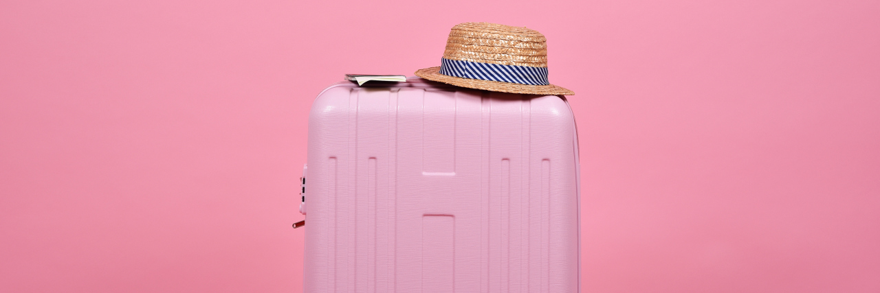 A light pink suitcase with a sun hat in front of a darker pink suitcase.