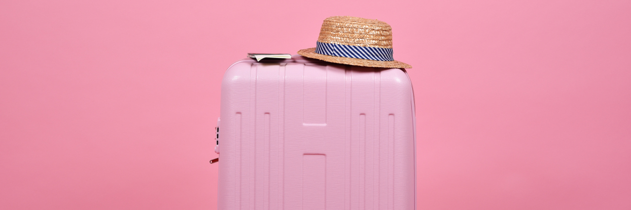 5 Things to Take on Holiday When You Have Chronic Pain A light pink suitcase with a sun hat in front of a darker pink suitcase.