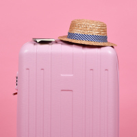 A light pink suitcase with a sun hat in front of a darker pink suitcase.