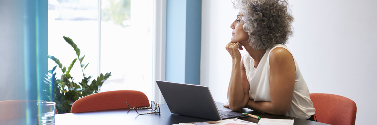 What It Feels Like When You Have to Stop Working Due to Illness Middle aged woman looking out of the window in the boardroom