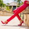 A picture of a woman's legs, wearing red pants and red stilettos outside.