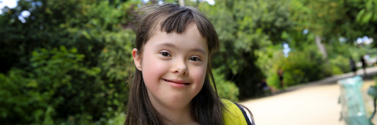 Girl with Down syndrome smiling at camera with a yellow backpack on