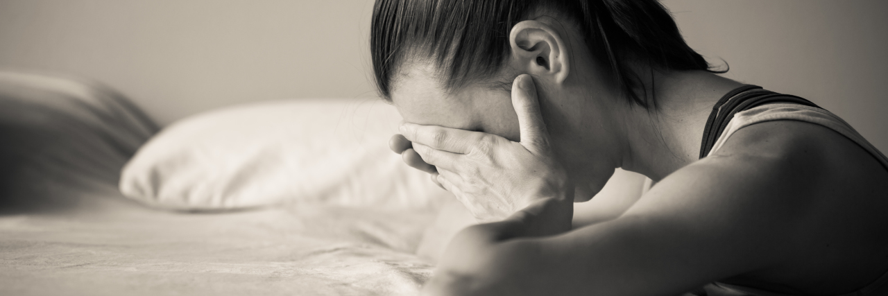Why It's OK to 'Drop My Sword' and Cry as a Parent Stressed woman with hand over face leaning on bed.
