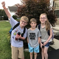 Three siblings posing forfirst day of school picture, one boy has Down syndrome