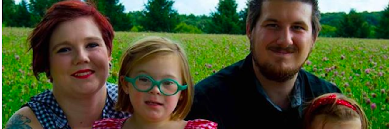 How My Daughter With Down Syndrome Helped Me Overcome Social Anxiety Family photo, mom, dad, and two daughters. The girls sit on their parent's laps.