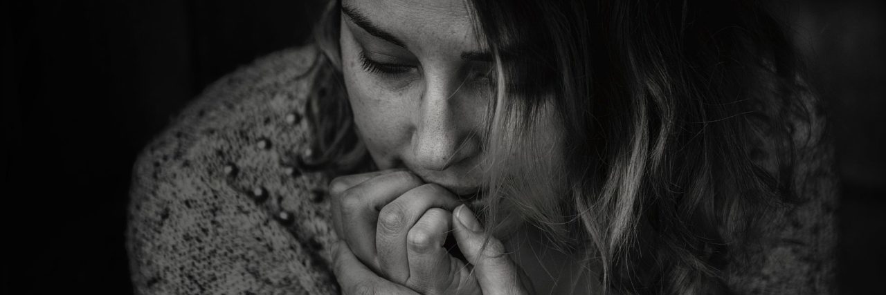 black and white photo of woman with fingertips to mouth looking down depressed