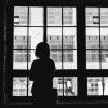 black and white photo of woman standing alone looking out a window