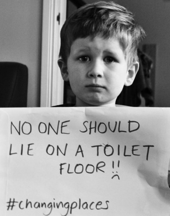 brody holding a sign saying "no one should lie on a toilet floor"