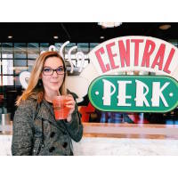 woman holding a drink and standing in front of central perk sign