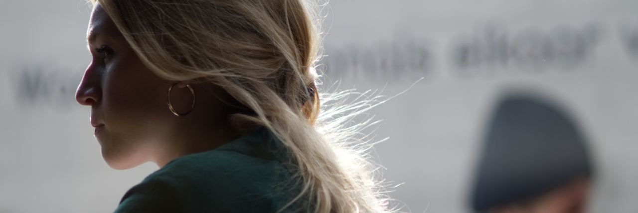 Having to Legitimize My Chronic Pain When Others Don't Believe Me blonde woman looking away, partially hidden in the shadows