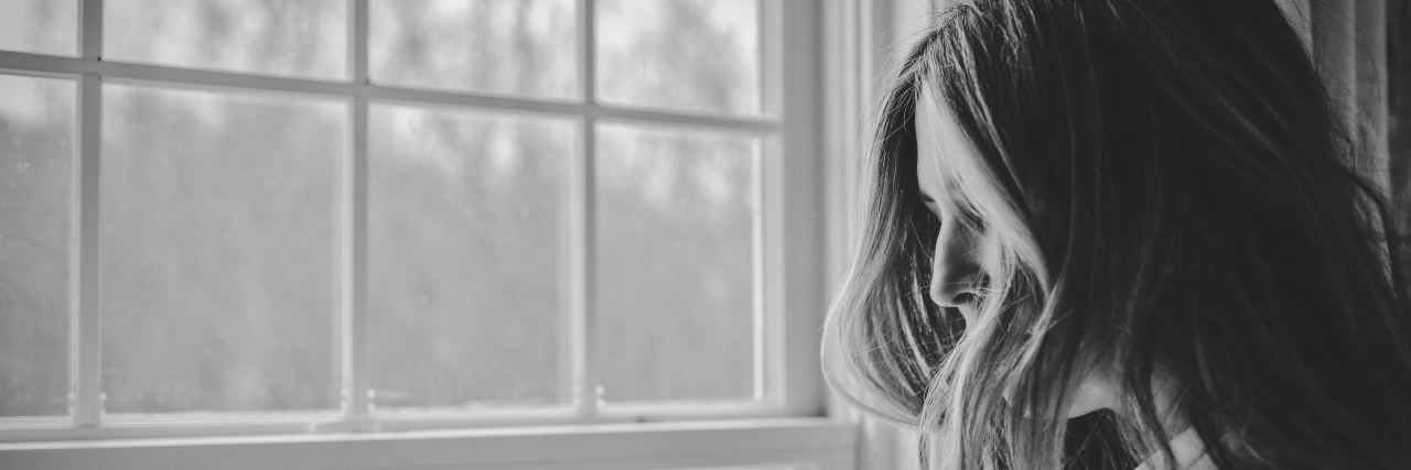 I'm Grieving the Life Fibromyalgia Took From Me A black and white image of a woman looking out the window, her hair covering most of her face.