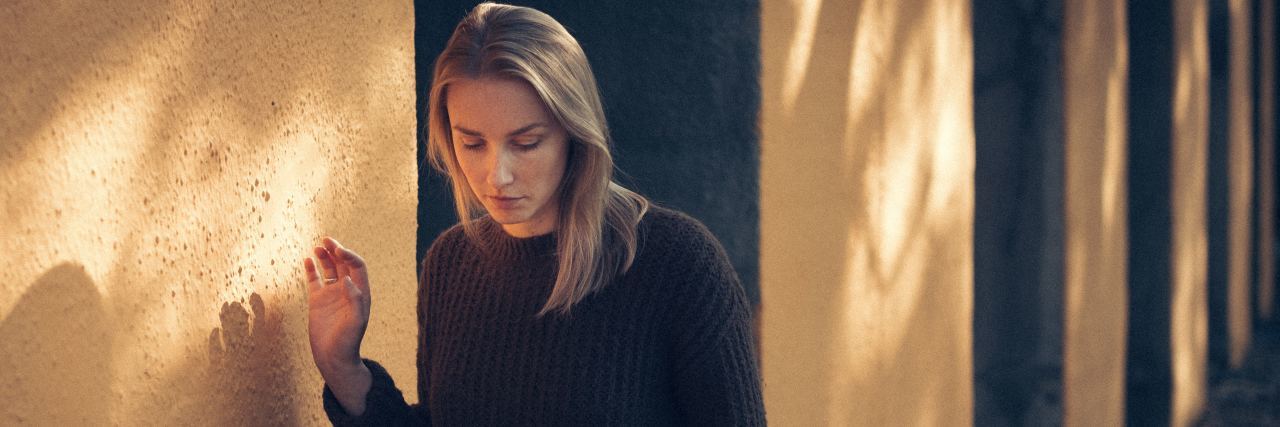 Why I Think Being Open About My Chronic Pain With Others Is a Bad Idea A woman outside, walking by a building.