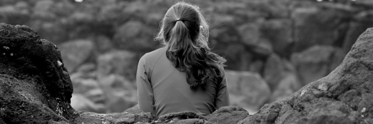 black and white photo of young woman sitting on rocks