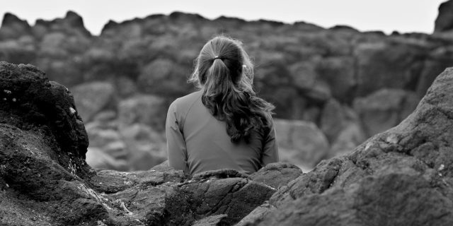 black and white photo of young woman sitting on rocks