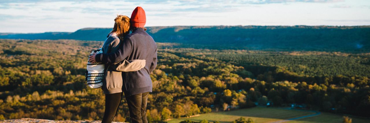 couple embracing in countryside looking over fields and trees
