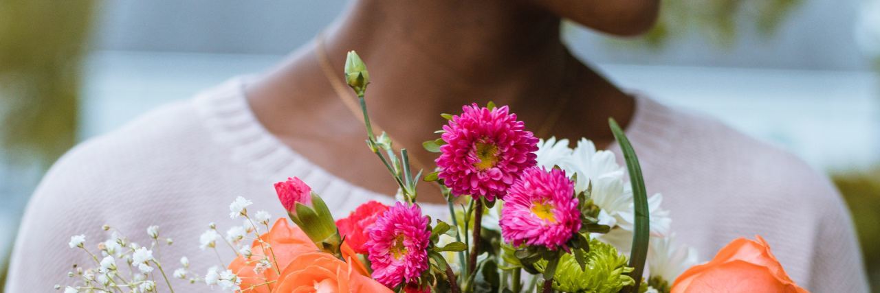 What Self-Care Really Means If Not Manicures and Pedicures woman holding pot of colorful flowers and smiling