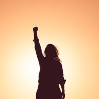 woman silhouette against sunset with arm and fist raised