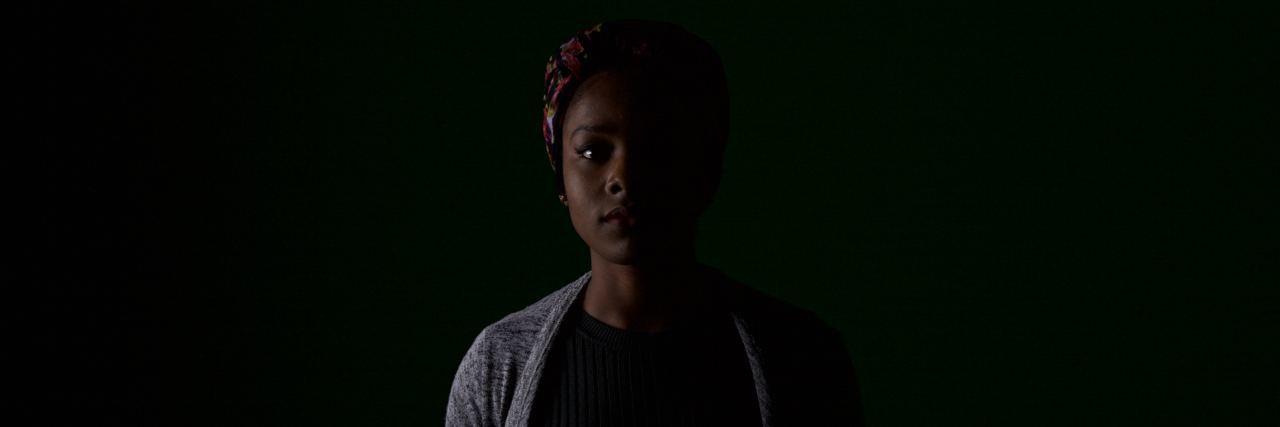 The Question No One Ever Asks About Life With Chronic Fatigue Syndrome A woman in a dark room, only showing part of her face and body.