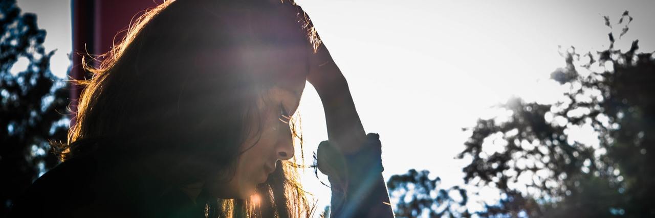 What It's Like Having an Invisible Illness and Not 'Looking Sick' woman putting hand on her head framed by sunny window