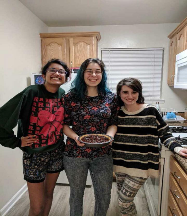 three girls smiling, one holding pie