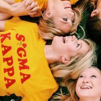 Sigma Kappa members laying in grass with yellow shirts with red letter that says "Sigma Kappa."