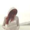 photo of woman wearing light color hooded sweater with hands in pockets and face hidden by red hair