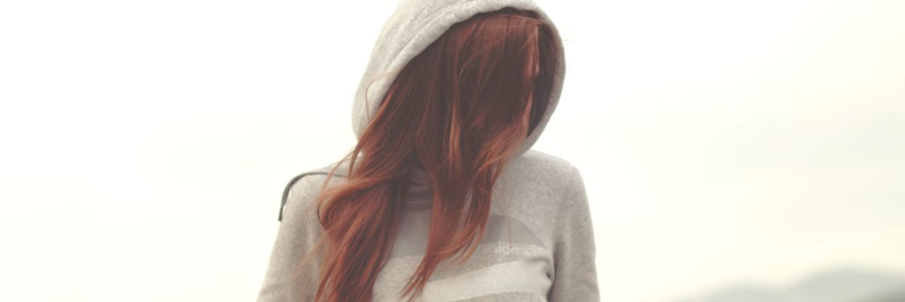 How to Recover From Gaslighting photo of woman wearing light color hooded sweater with hands in pockets and face hidden by red hair