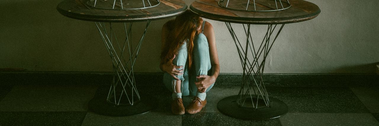 woman hugging knees under tables against wall
