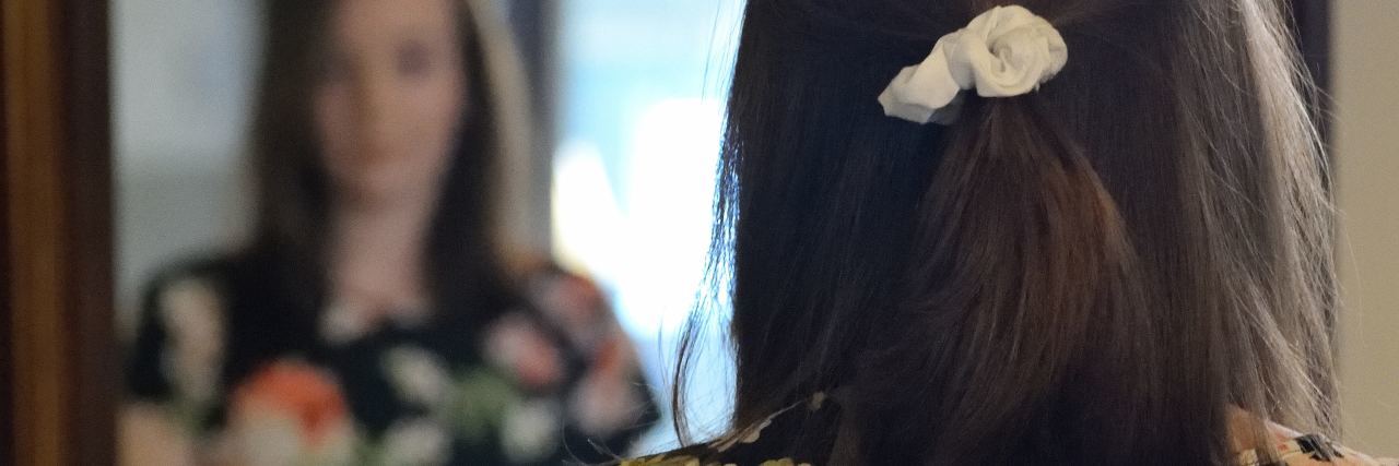 Eating Disorder Recovery Symptoms to Be Prepared For young woman looking at herself in full length mirror wearing floral top and jeans