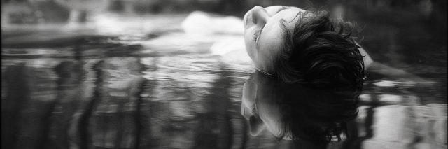 woman lying in water in forest with reflection