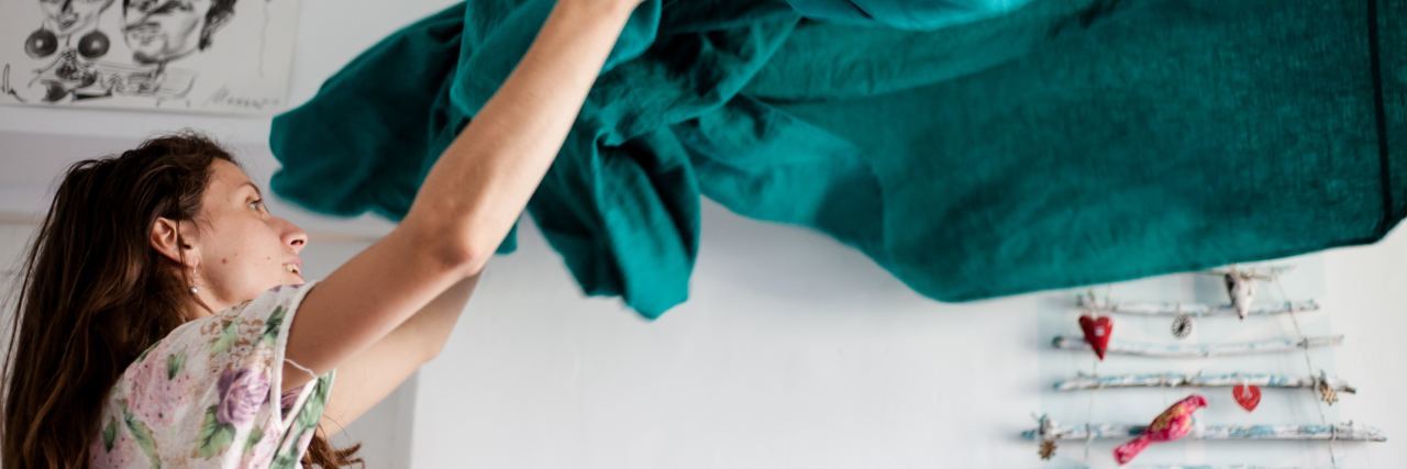 photo of woman making bed with turquoise color sheet in air