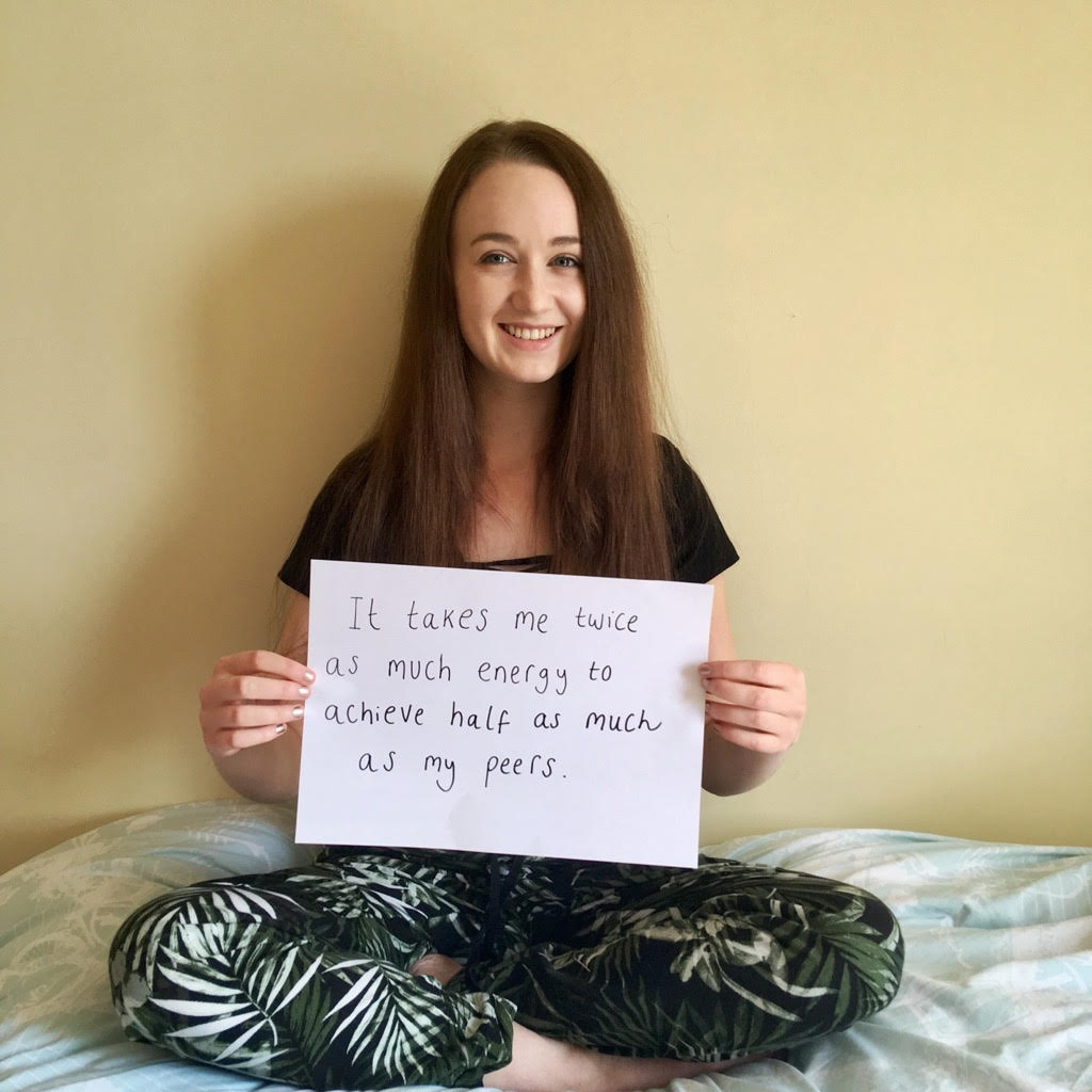 Pippa on bed holding sign that reads 'it takes me twice as much energy to achieve half as much as my peers'