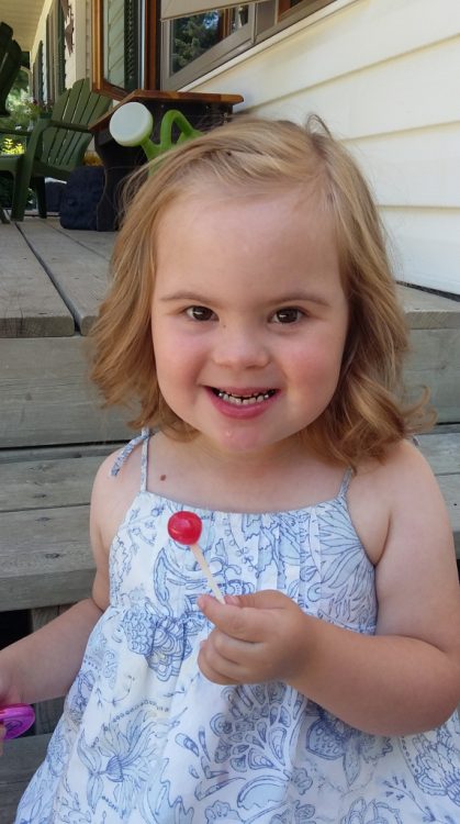 Little girl with Down syndrome smiling at camera holding red lollipop