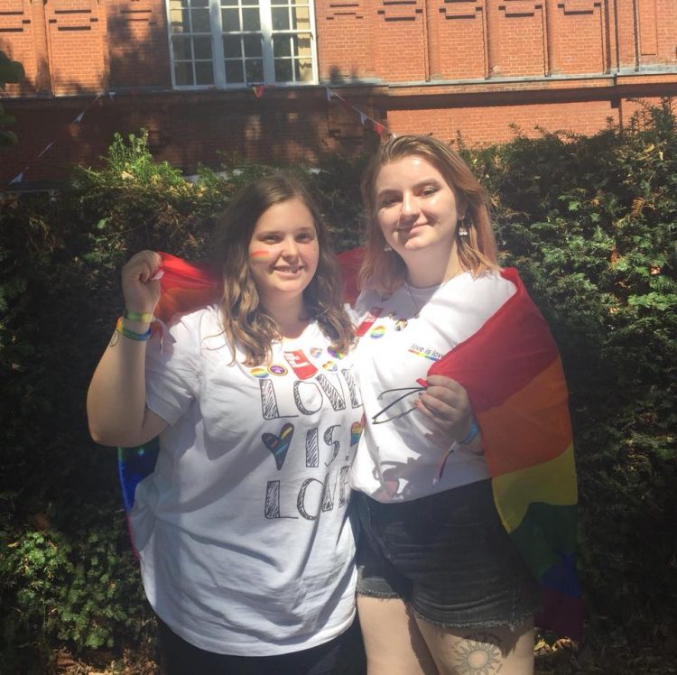 two woman posing with pride flag 