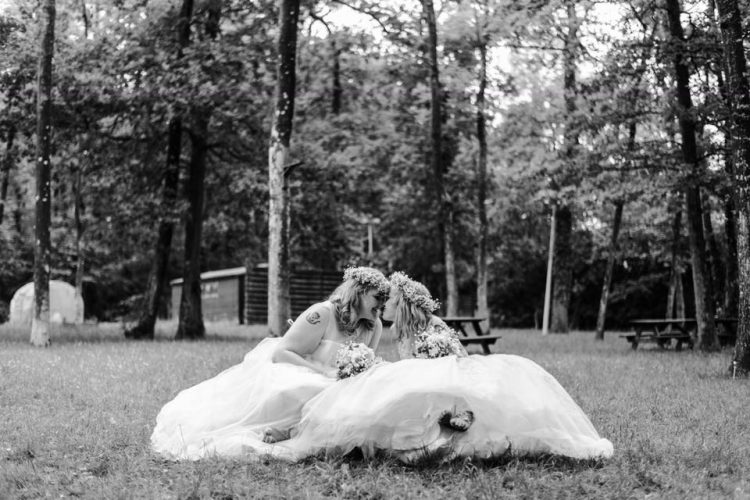 two brides sitting on grass surrounded by trees