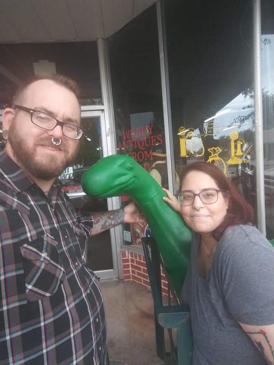 man and woman standing outside store with inflatable dinosaur