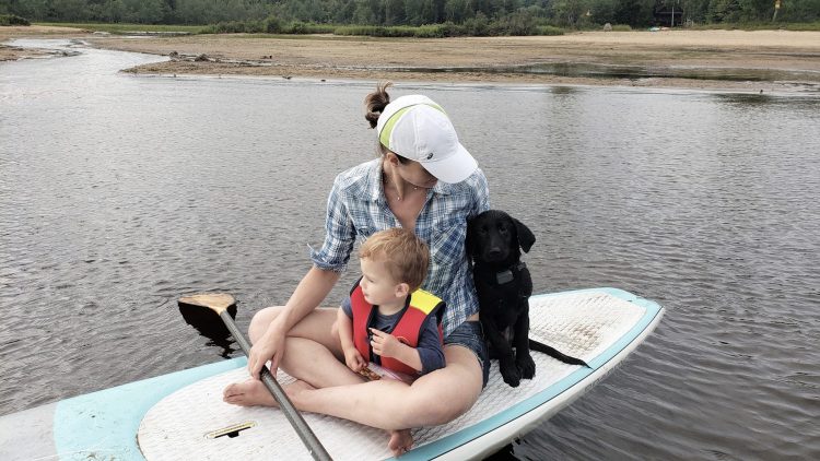woman sitting with baby and dog on stand up paddleboard